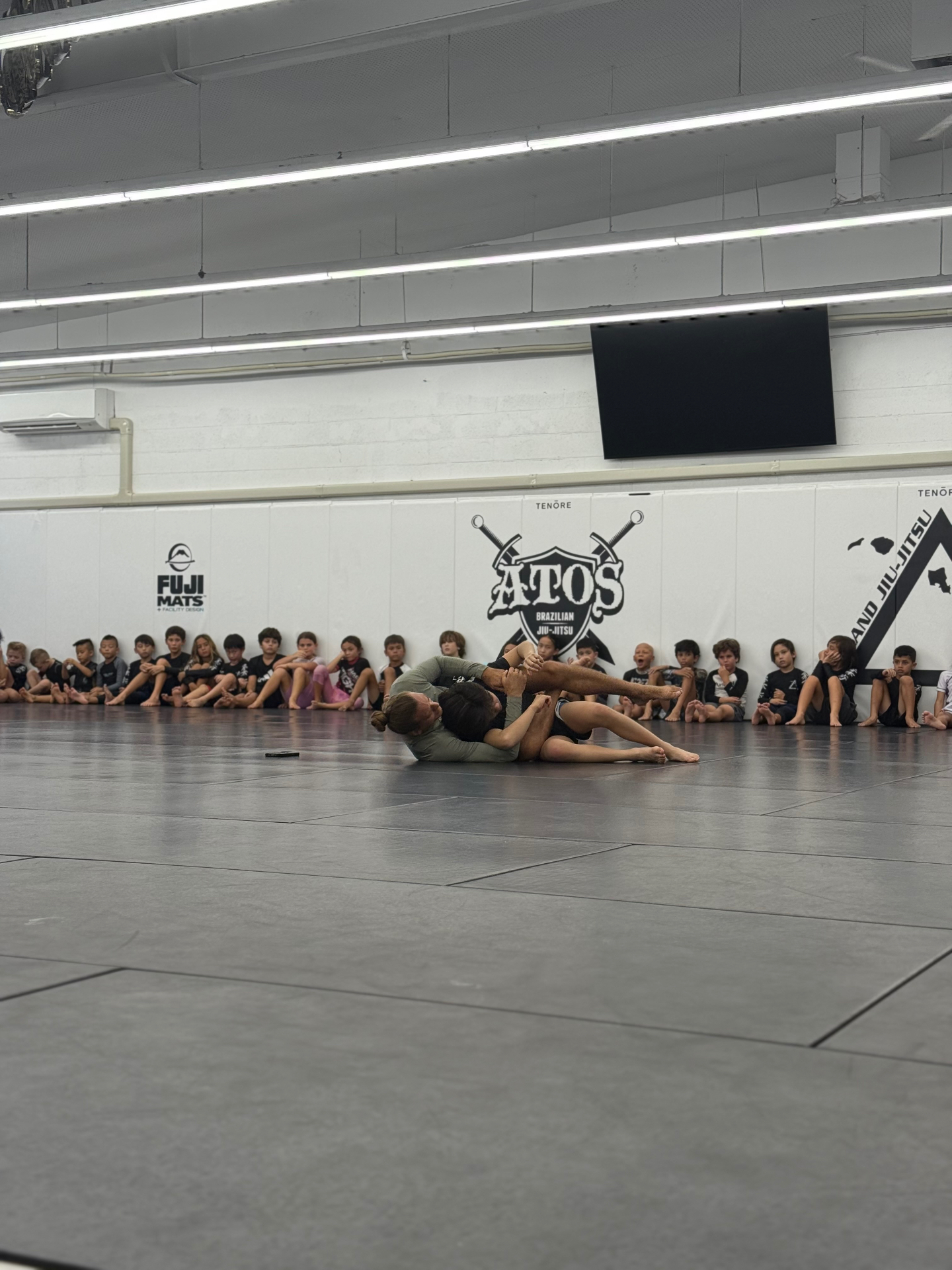 Kids watching a jiu-jitsu technique demonstration on the mats